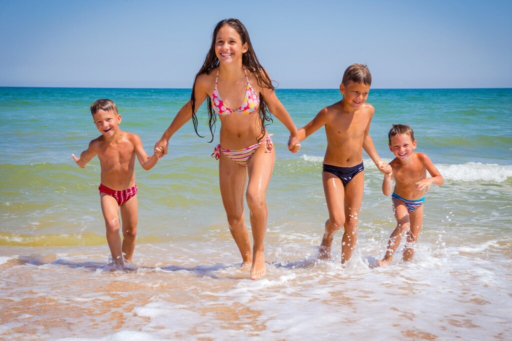 Una donna e tre bambini felici corrono sulla spiaggia verso il mare.