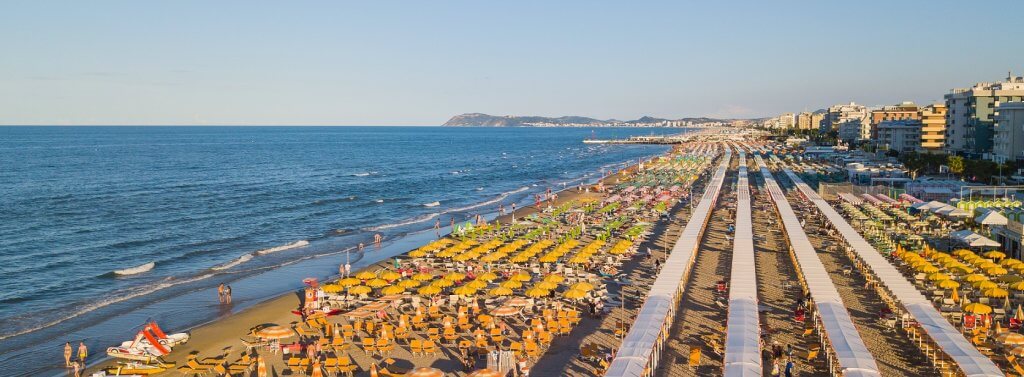 Spiaggia affollata con file di ombrelloni gialli vicino al mare.