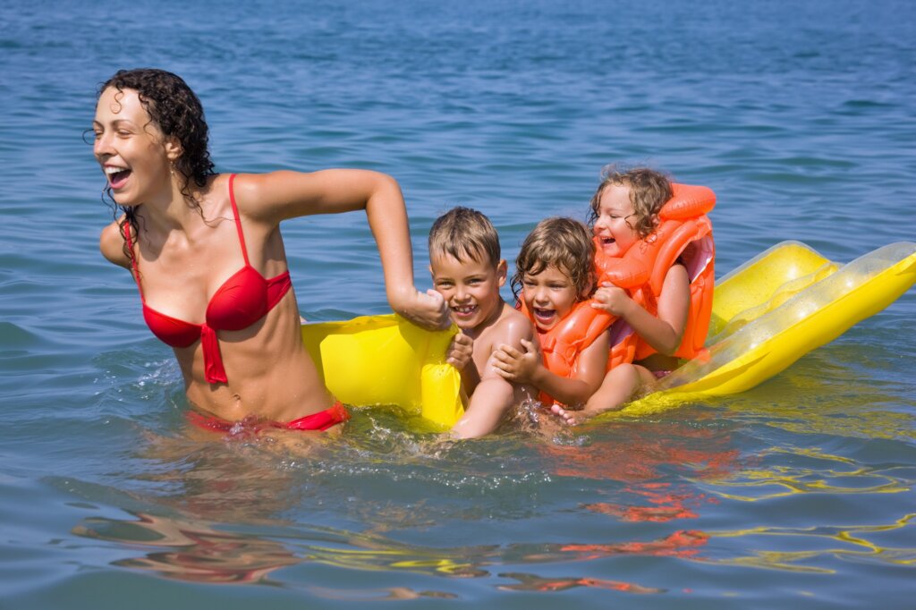 Una donna e tre bambini sorridenti si divertono in mare con un materassino giallo.