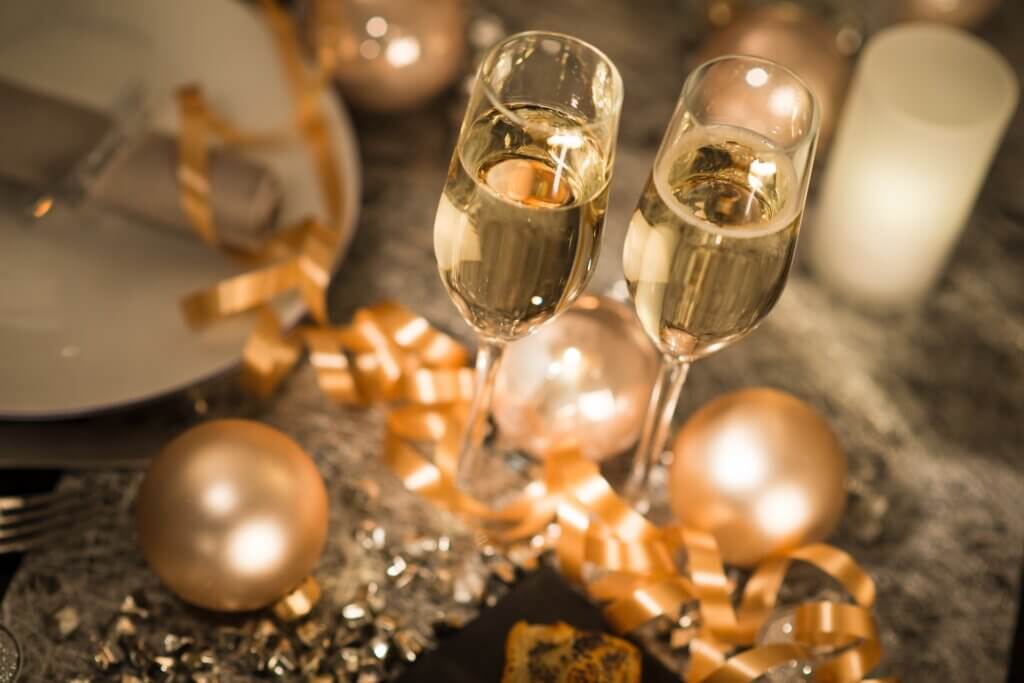 Calici di champagne su tavola elegante decorata con palline e nastri dorati.
